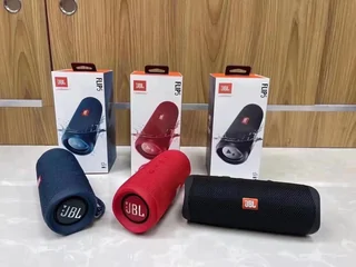 Five cylindrical bluetooth speakers in black, red and blue with their boxes