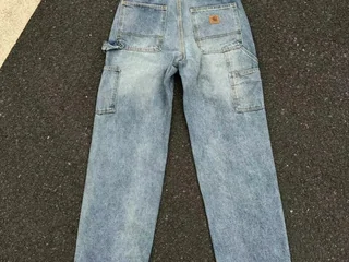 A pale blue washed loose-fit pair of jeans laid flat on concrete
